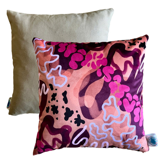 The front and back of the Sunset cushion by Beth Morgan Art. It features swirling shapes and abstract prints in shades of orange, pink and purple. The back is a plain beige fabric.