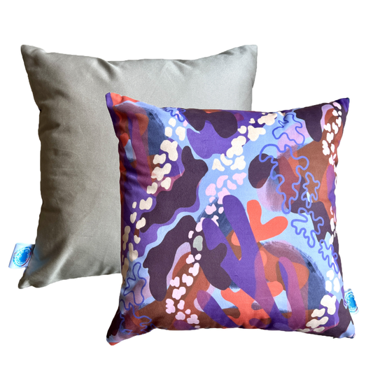 The front and back of Blossom, a soft velvet statement cushion. The front features large and small abstract shapes in differing shades of purple, orange and pink. The back is a plain beige colour.