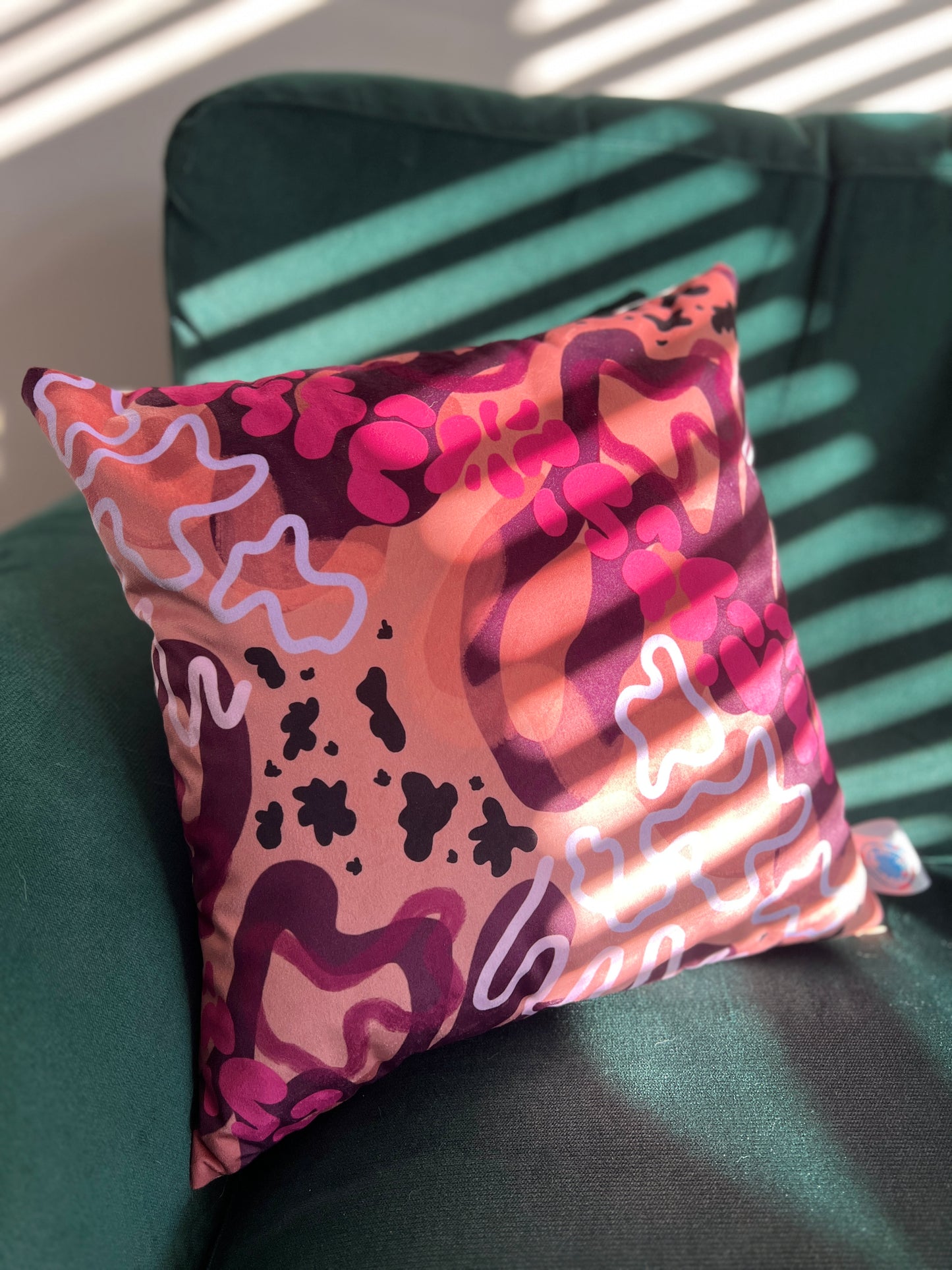 Bands of sunlight across a vibrant cushion featuring abstract shapes of oranges, pinks and purples on a green sofa.