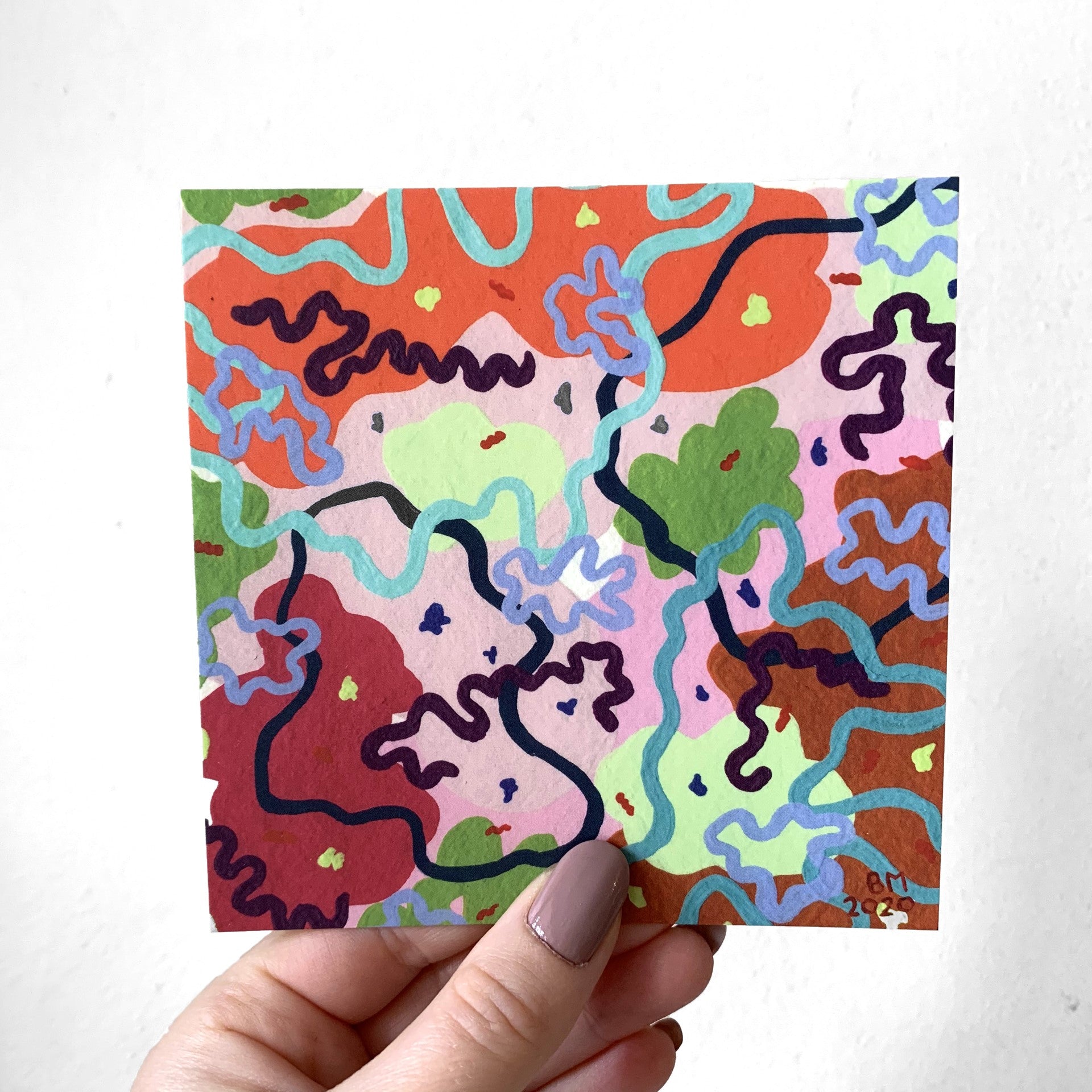 A hand holding a colourful abstract print in front of a white wall. The print it made of abstract prints in vibrant colours. 